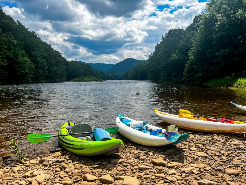 Inflatable kayaks resting on rocky riverbank with forested hills and wide river view